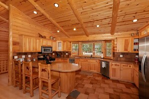 A wooden cabin interior with a kitchen area featuring a central island, wooden cabinets, and a stainless steel refrigerator.
