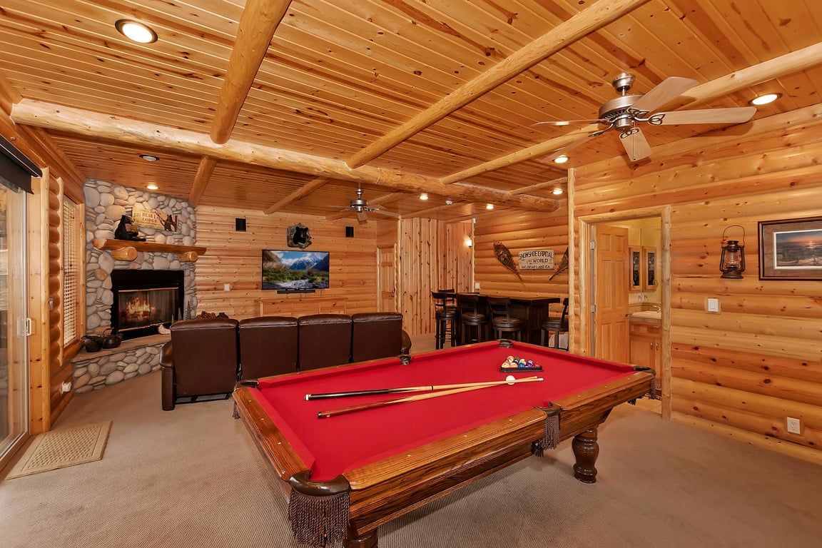 Ein Holzinterieur mit Billardtisch, einer Sitzecke, Kamin und Deckenventilator.