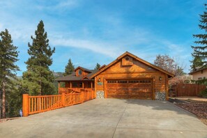 A log cabin with a garage, a covered porch, and a fenced driveway.