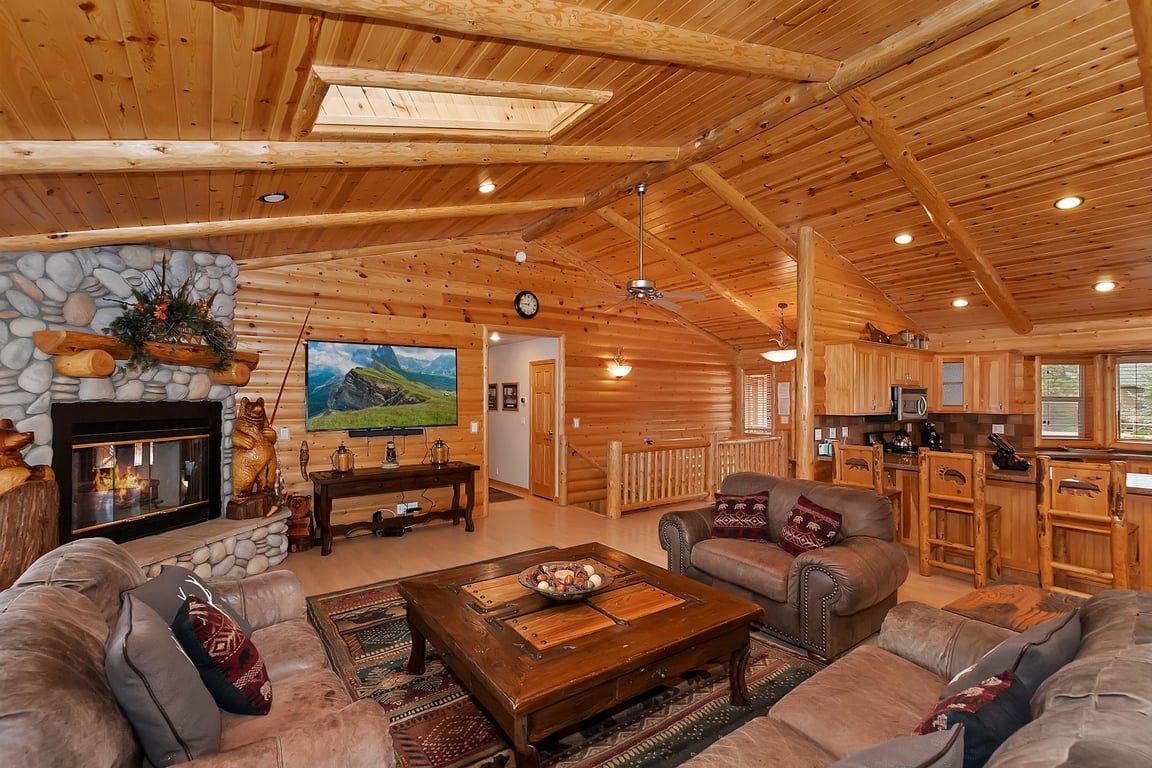 Un salon spacieux avec une cheminée en pierre, des canapés en cuir, une table basse et un grand tableau représentant un paysage de montagne.
