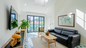 A modern living room with a black leather sofa, a wooden coffee table, and a large window with a view of the outdoors. - w* | Spacious 1BR in Santa Ana (Panamá)