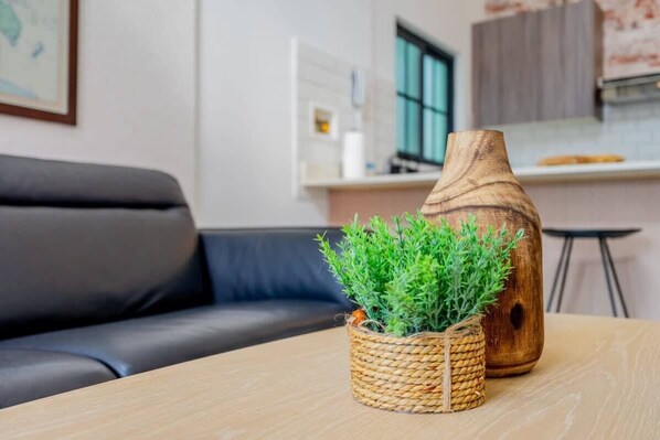 A living room with a dark leather sofa, a wooden table with a woven basket containing green plants, and a wooden vase.