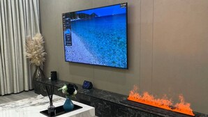 Ein modernes Interieur mit einem Marmor-Rezeptionstresen, einem montierten Fernseher, der eine Strandansicht zeigt, und einer dekorativen Feuerstelle.