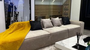 Ein modernes Wohnzimmer mit einem beigen Sofa, einer gelben Decke und einem Couchtisch aus Marmor.