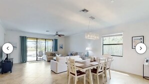 Un salon spacieux comprenant un coin repas, de grandes fenêtres et un ventilateur de plafond.