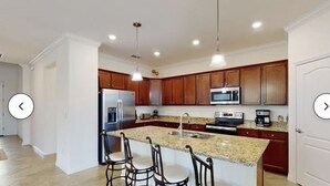 Une cuisine moderne dotée de plans de travail en granit, d’appareils électroménagers en acier inoxydable, d’armoires en bois et de luminaires suspendus.