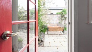 Une porte rouge qui donne sur un patio avec un banc en bois et un mur en briques.