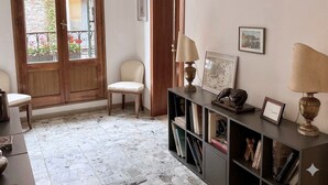 Una habitación con puerta de madera, una silla, una estantería con libros y objetos decorativos, y una ventana que ofrece vistas al exterior.