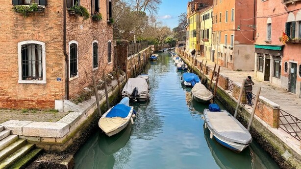 Un canal estrecho bordeado por edificios históricos con ventanas de arco y una hilera de barcos amarrados a la orilla.