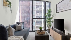 Una sala de estar moderna con un sofá, una mesa de centro, un televisor y ventanas amplias.