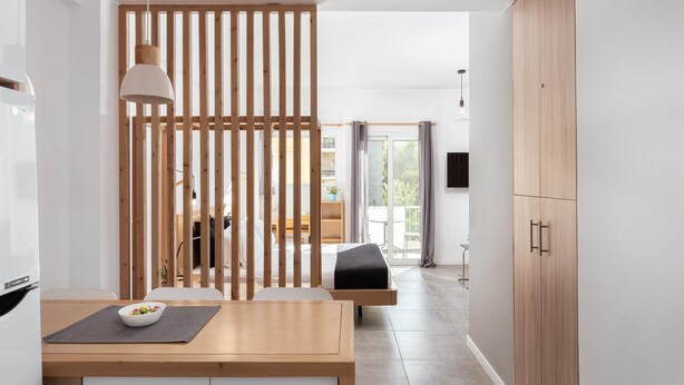 A modern, minimalist room with a wooden partition, a bed, a dining table with a bowl of fruit, and a wardrobe. - Acropolis Cozy Living (Athina)