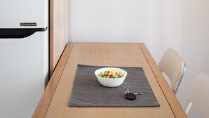 A kitchen with a white refrigerator, a wooden table with a bowl of fruit, and a pendant light. - Acropolis Cozy Living (Athina)