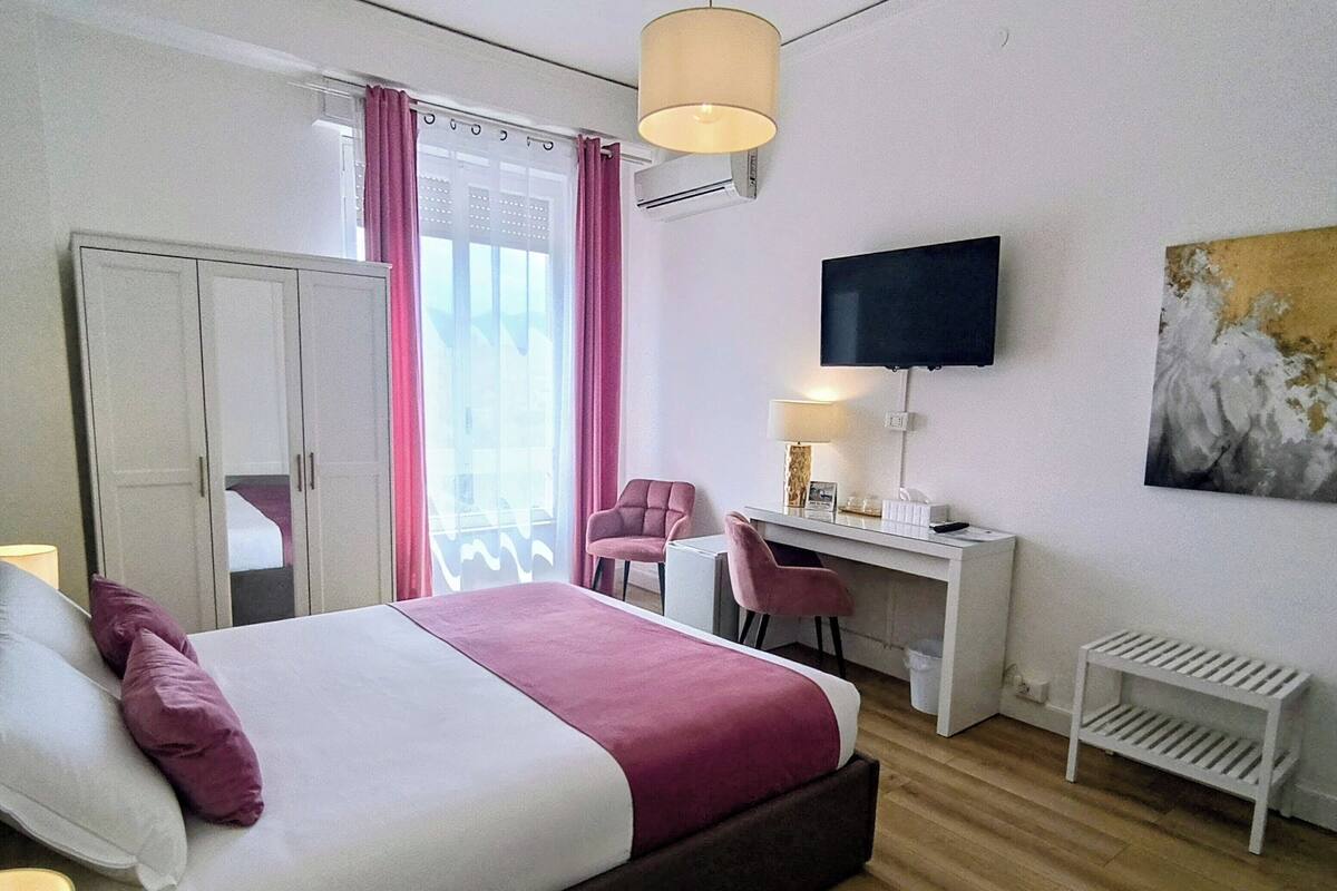 A bedroom with a bed, desk, chair, TV, wardrobe, and artwork.