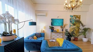 En moderne stue med blå sofaarrangement, en lysekrone og et fladskærms-tv.
