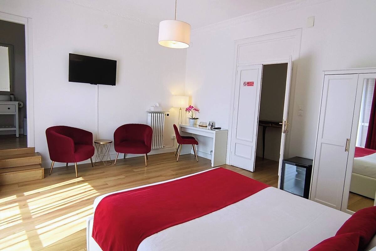 A hotel room with a bed, two red chairs, a desk, a television, and a wardrobe.