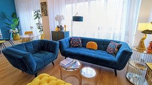 En moderne stue med en blå sofa, en gul fodskammel og et rundt sofabord.