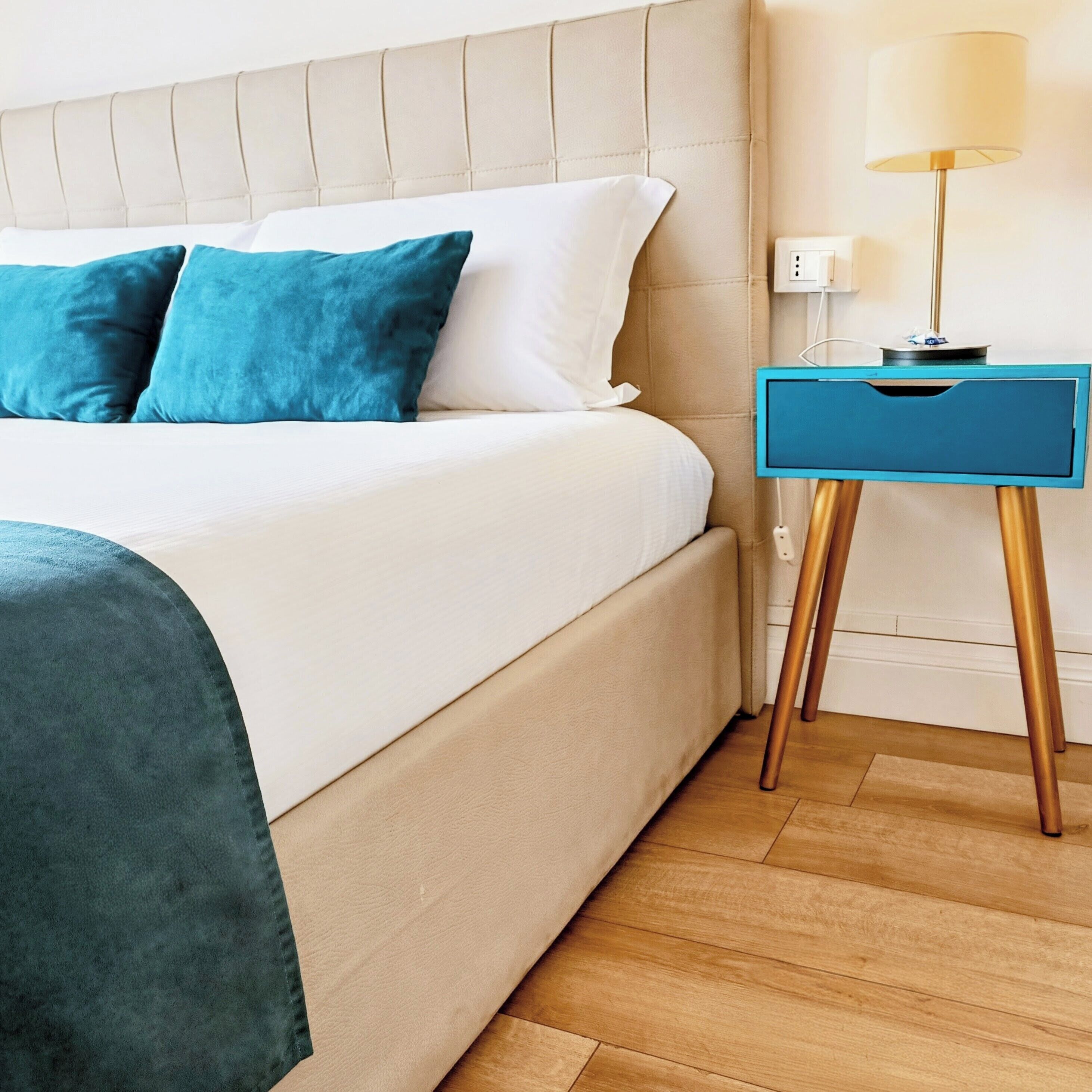 A bed with a headboard, a bedside table with a lamp, and a wall socket.