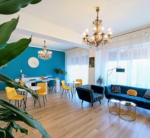 Una sala de estar moderna con una pared azul de acento, una araña, un sofá y un comedor con sillas amarillas.