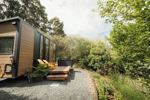 A modern, compact house with a wooden exterior, a small deck, and a gravel pathway leading to the entrance. - Tranquility Tiny House by Tiny Away (Owaka)