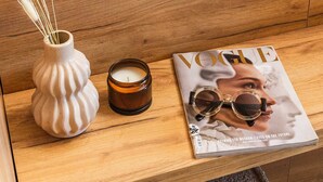 A neatly arranged bedroom with a wooden headboard, a white bed with a black pillow, a vase with feathers, a candle, and a magazine on a wooden nightstand. - Skiathos Avaton Garden (Skiathos)