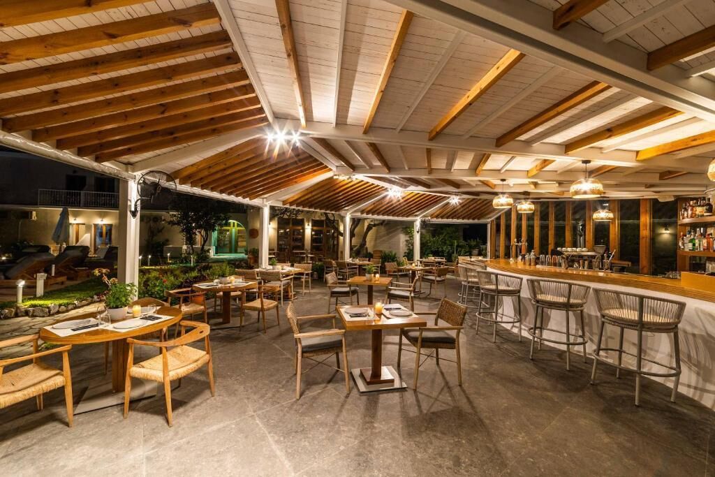An outdoor dining area with wooden tables and chairs, a bar, and a covered seating area with a view of the garden.