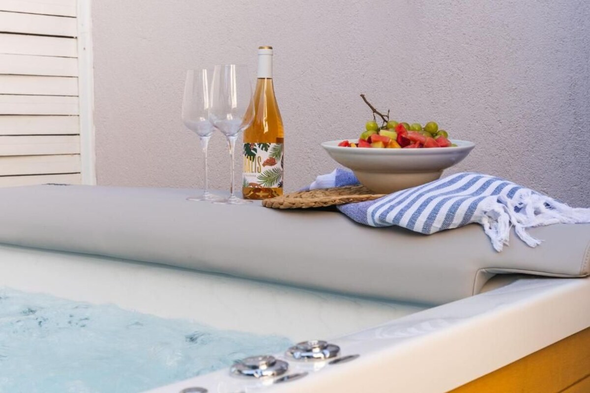 A spa area with a bathtub, two glasses of wine, a bottle of wine, and a bowl of fruit.