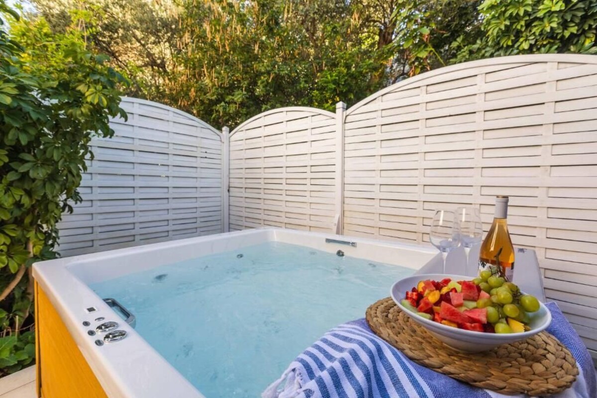 A hot tub with a bowl of fruit and a bottle of wine on a mat.