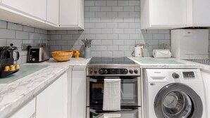 A modern kitchen with white cabinets, a stainless steel stove, a washing machine, and a tiled backsplash. - Central & Stylish 1BD Flat - 8mins to Greenwich! (London)