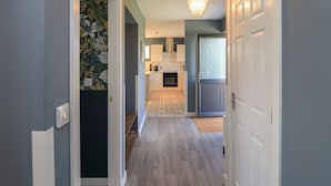 Un corridoio che conduce a una cucina con un tappeto decorato, un lampadario e una porta con pannello in vetro satinato.