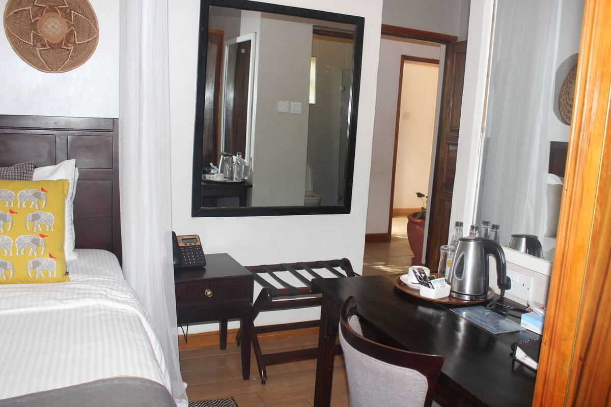 A hotel room with a bed, a desk, a chair, a large mirror, and a coffee maker.