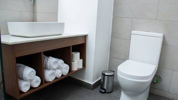 Un baño con lavamanos blanco, tocador de madera, espacio para toallas, inodoro y basurero.