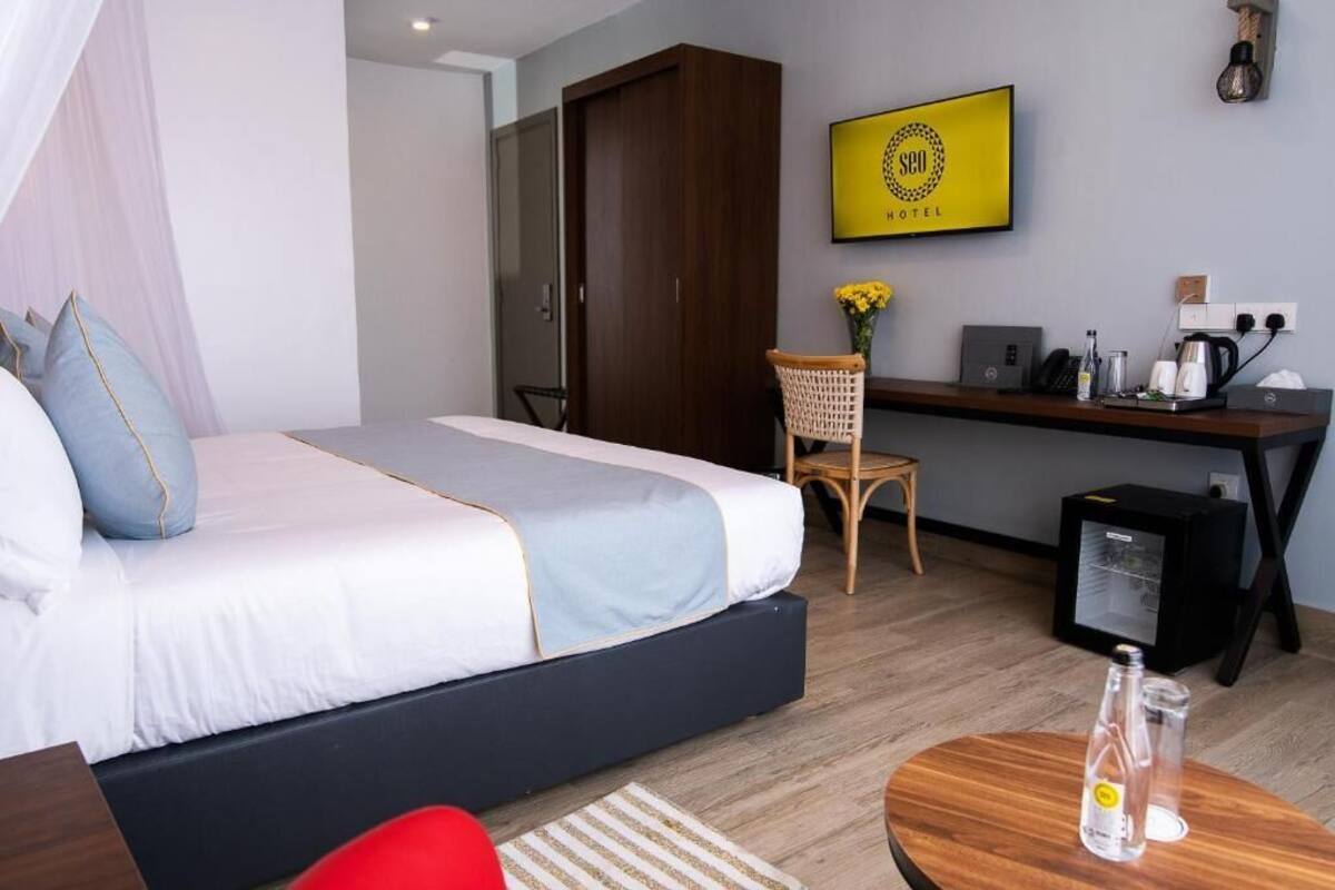 A hotel room with a bed, a desk, a chair, a small table, and a wall-mounted TV.