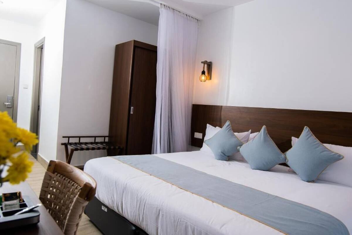 A hotel room with a bed, a wardrobe, a desk with a chair, and a wall-mounted light fixture.