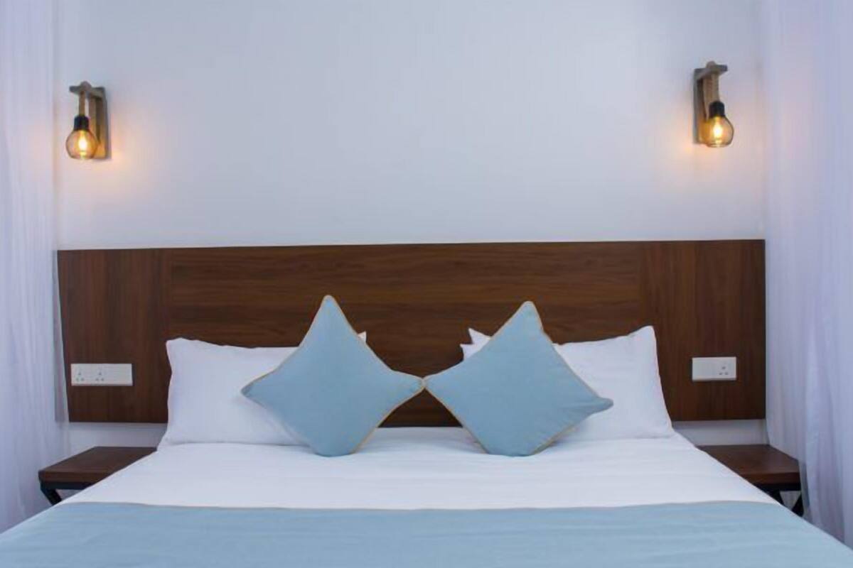 A neatly made bed with a wooden headboard, two bedside tables, and two wall-mounted light fixtures.