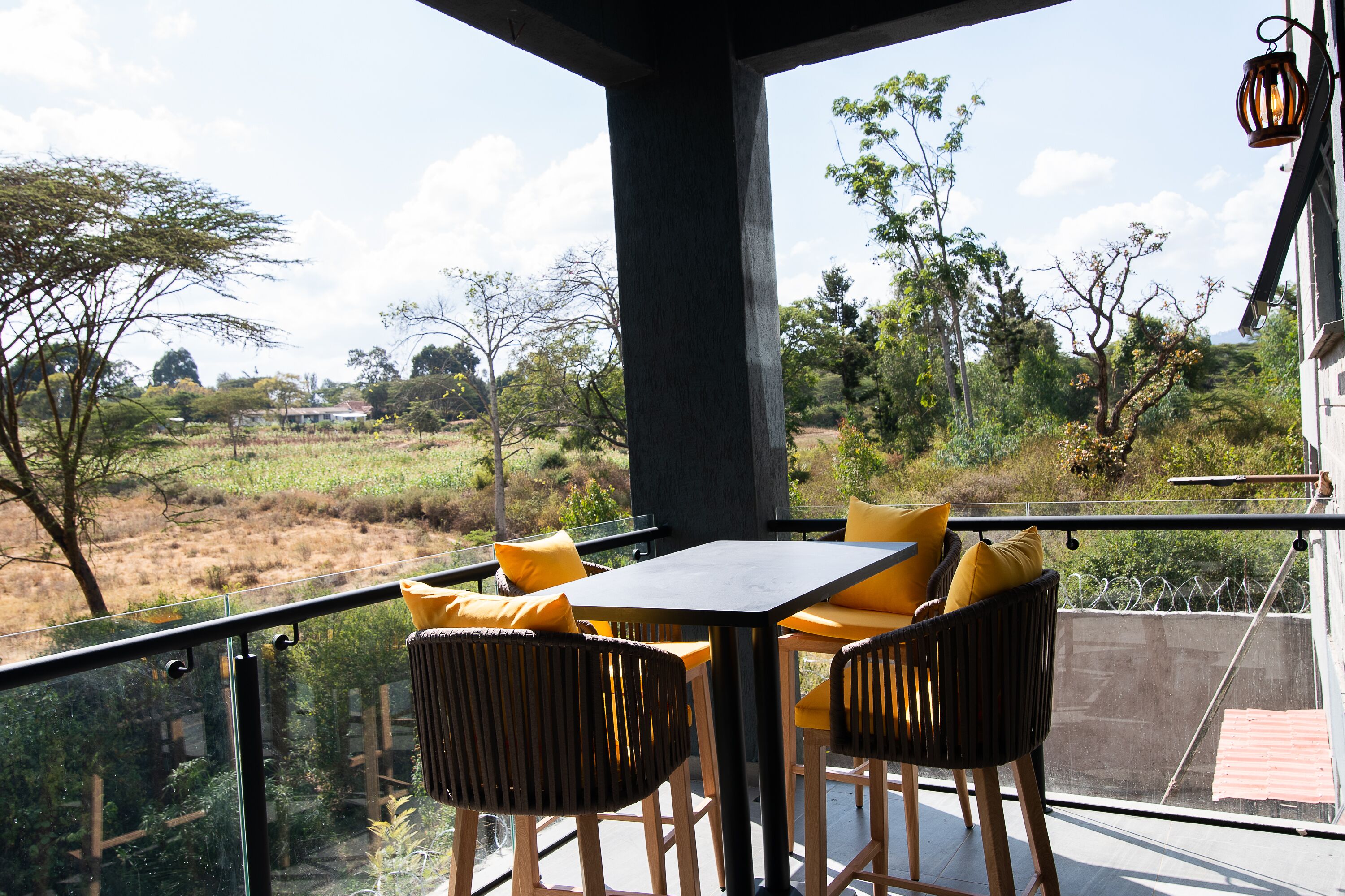 Een balkon met een tafel en stoelen, met uitzicht op een natuurlandschap met bomen en een veld.