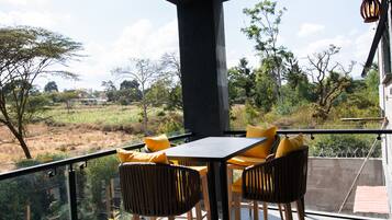 Un balcón con una mesa y sillas, con vista a un paisaje natural con árboles y un campo.
