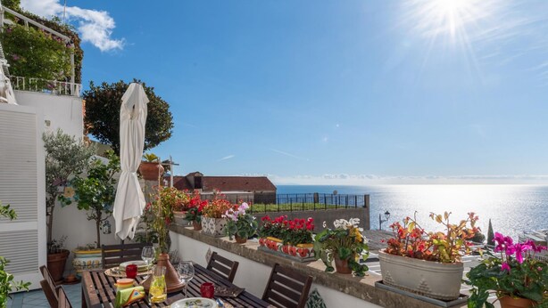 A terrace with a table set for dining, potted plants, and a view of the sea. - Casa Peppenella in Positano (Positano)