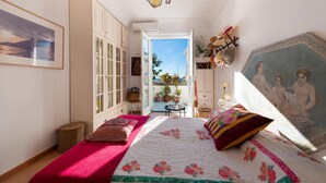 A bedroom with a bed, a painting, a wardrobe, and a view of the outdoors. - Casa Peppenella in Positano (Positano)
