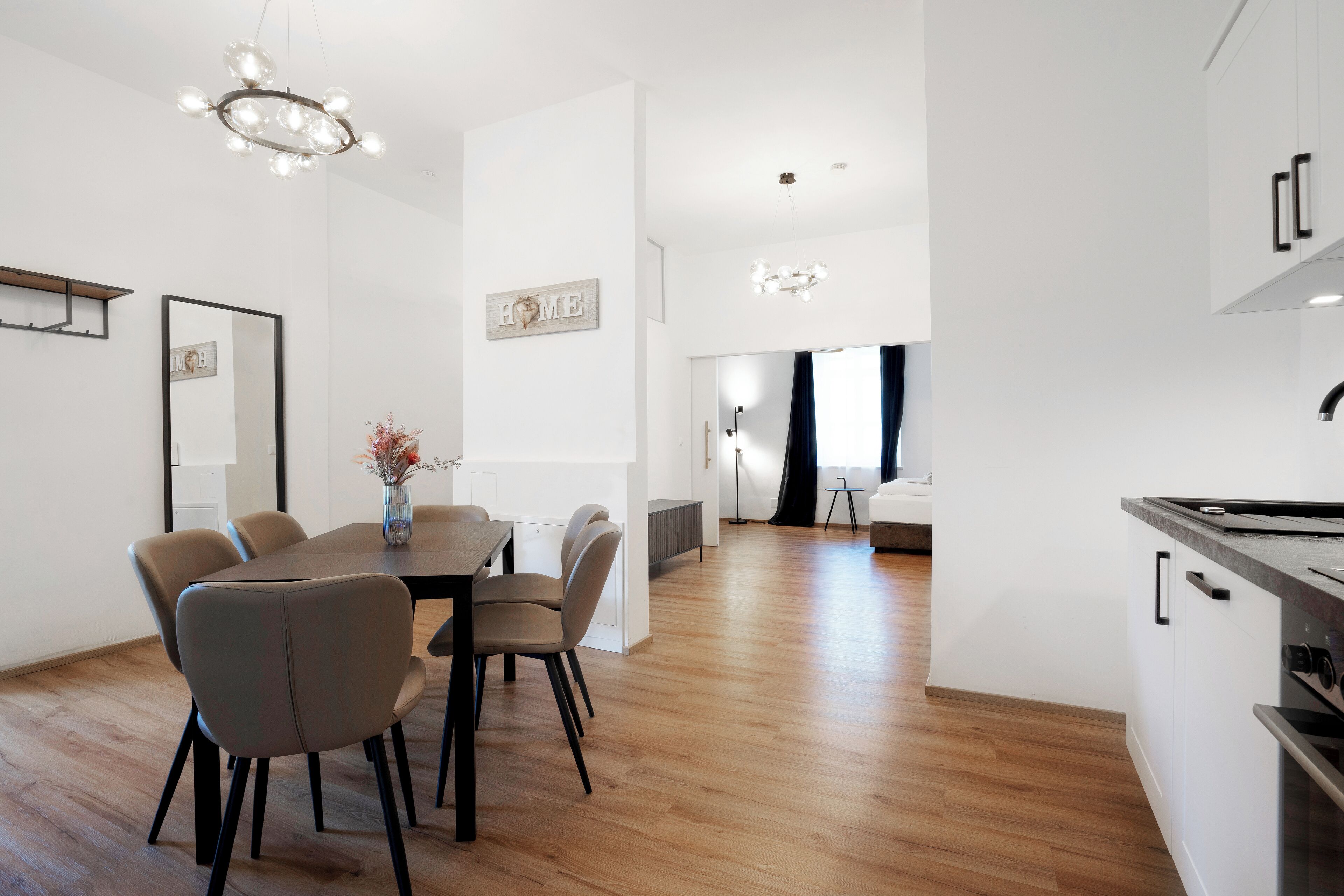 Een moderne keuken met een ingebouwde kookplaat, houten vloer en een eethoek met een tafel en stoelen.