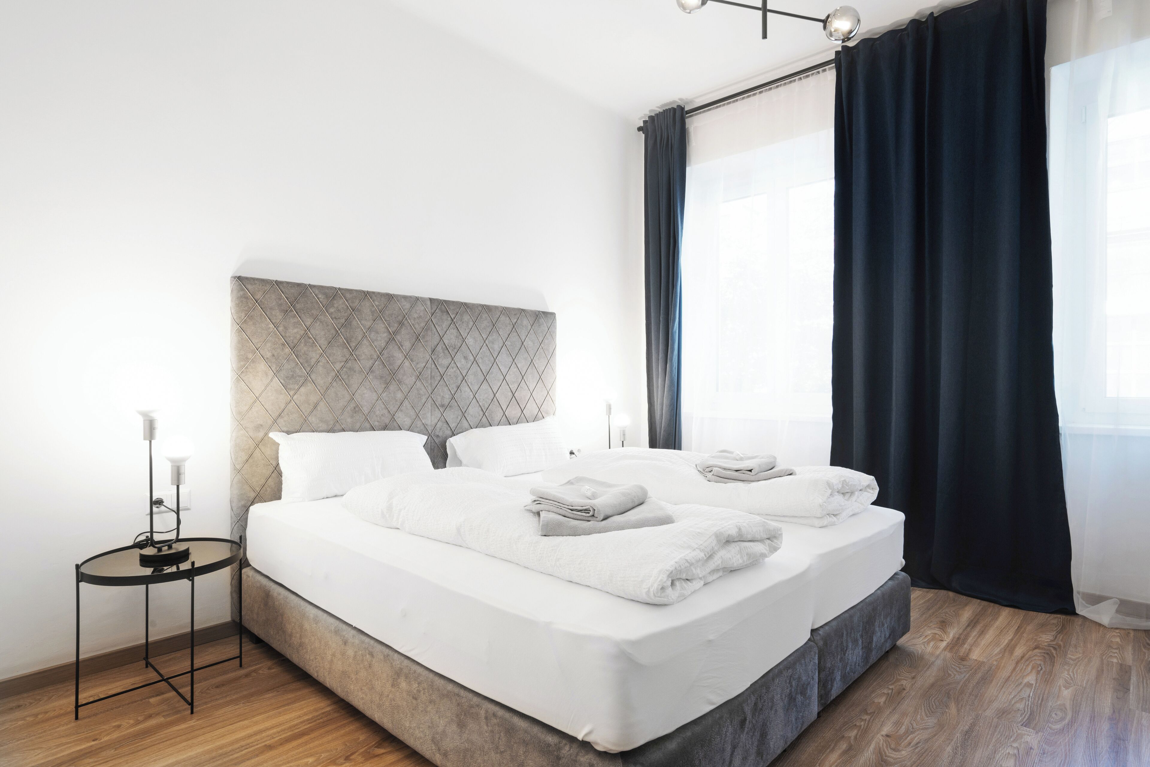 Ett modernt hotellrum med en stor säng, ett sängbord med en lampa och utsikt över omgivningarna genom ett fönster med gardiner.