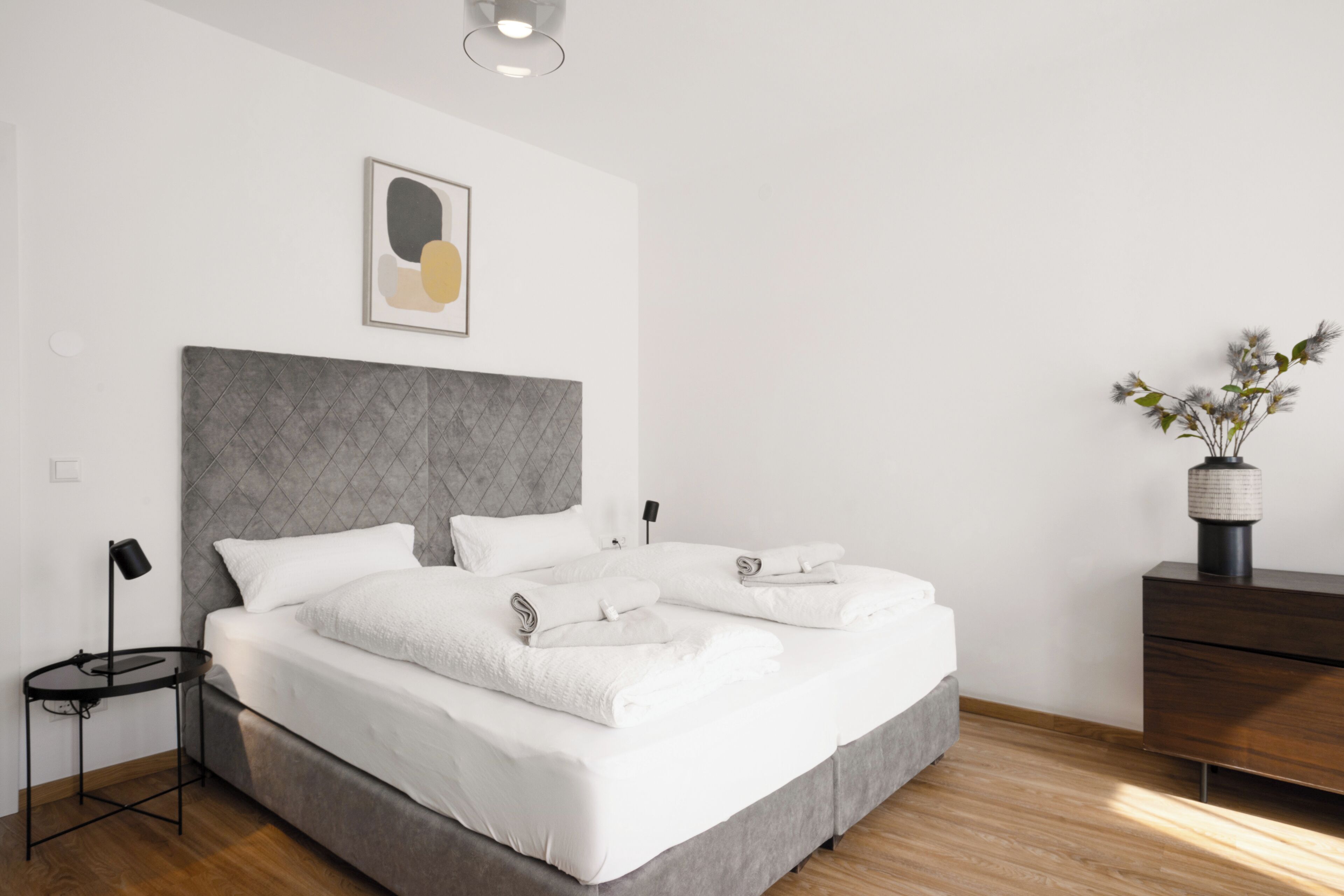 Een moderne slaapkamer met een groot bed, een nachtkastje, een lamp, een dressoir en een kunstwerk aan de muur.