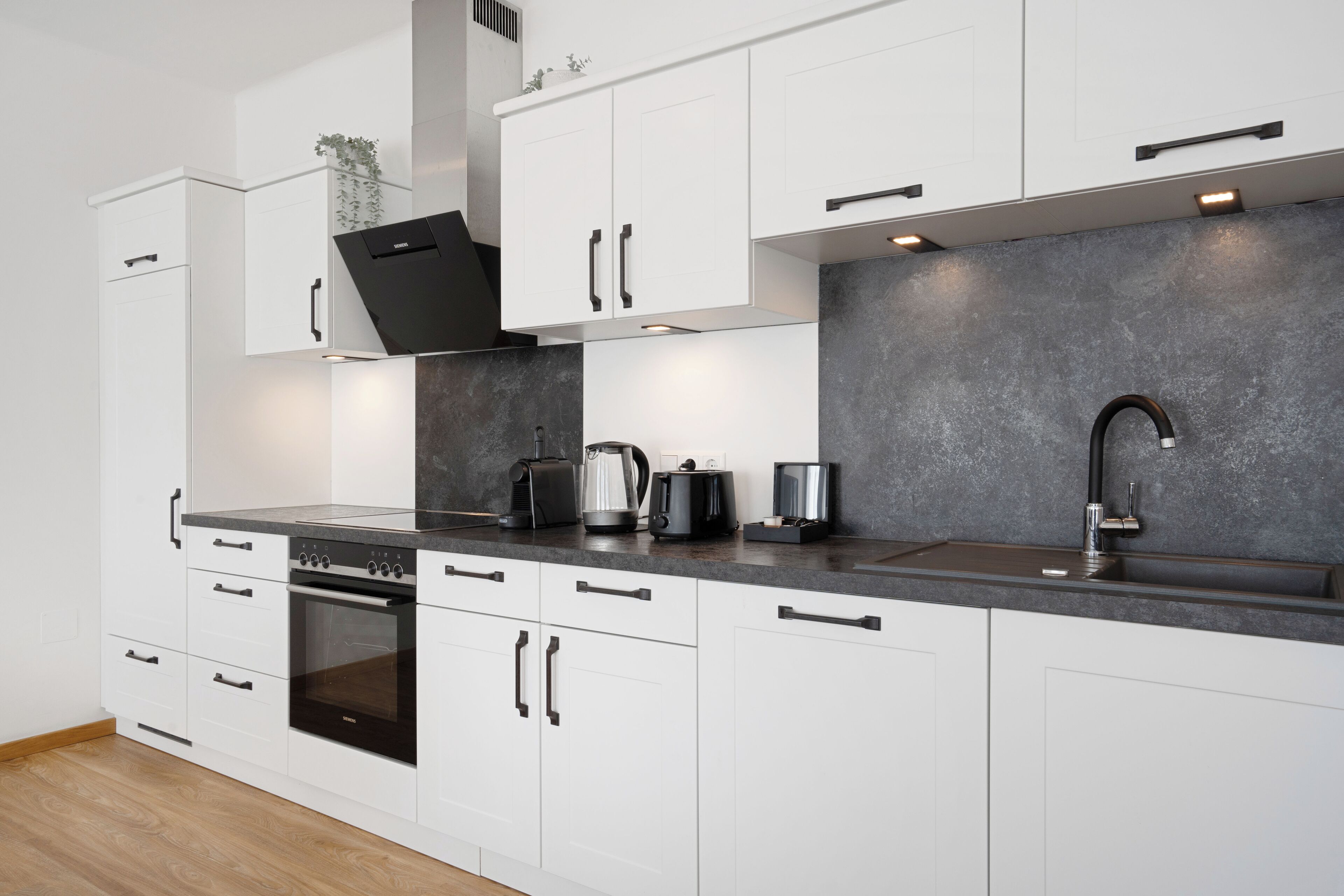 Una cocina moderna con armarios blancos, una estufa negra, un lavamanos y una encimera con cafetera y hervidor.
