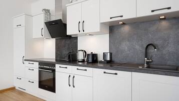 Una cocina moderna con armarios blancos, una estufa negra, un lavamanos y una encimera con cafetera y hervidor.