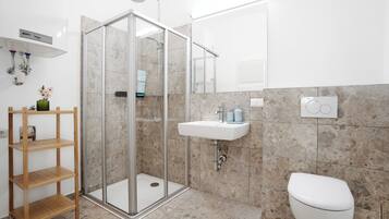 Een moderne badkamer met een douchecabine van glas, een witte wastafel en een toilet.