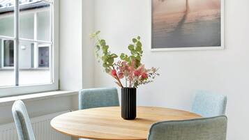 A round wooden table with a black vase containing flowers, surrounded by light blue upholstered chairs.