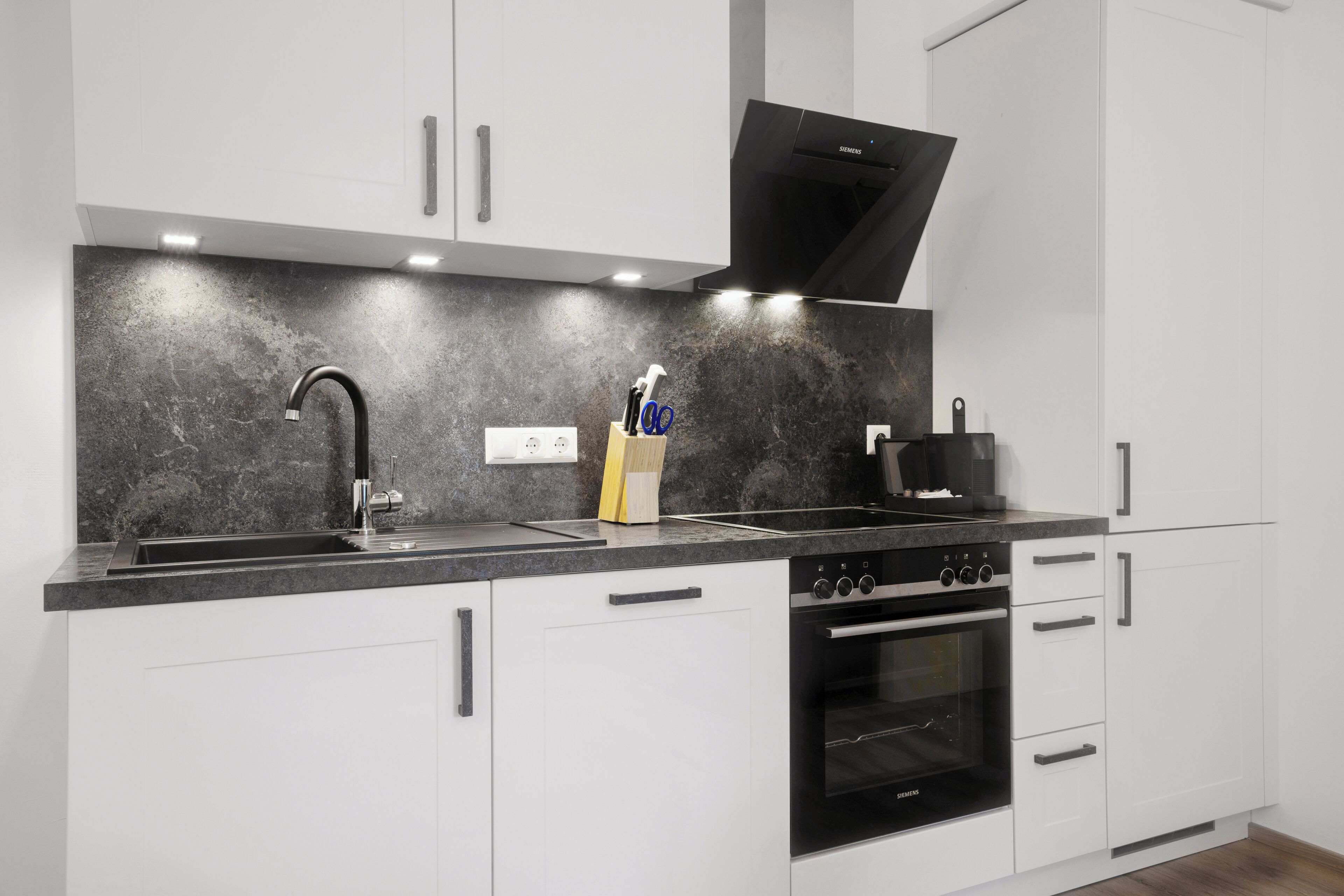 A modern kitchen with a black faucet, a built-in oven, and white cabinetry.
