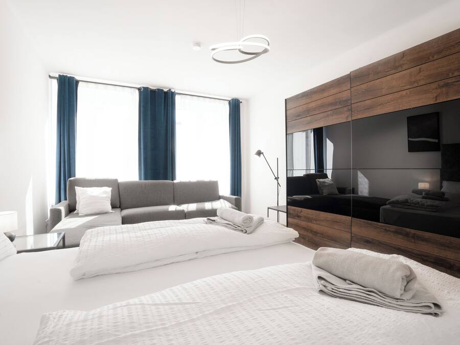 A modern hotel room with a large bed, a sofa, a desk, and a TV.