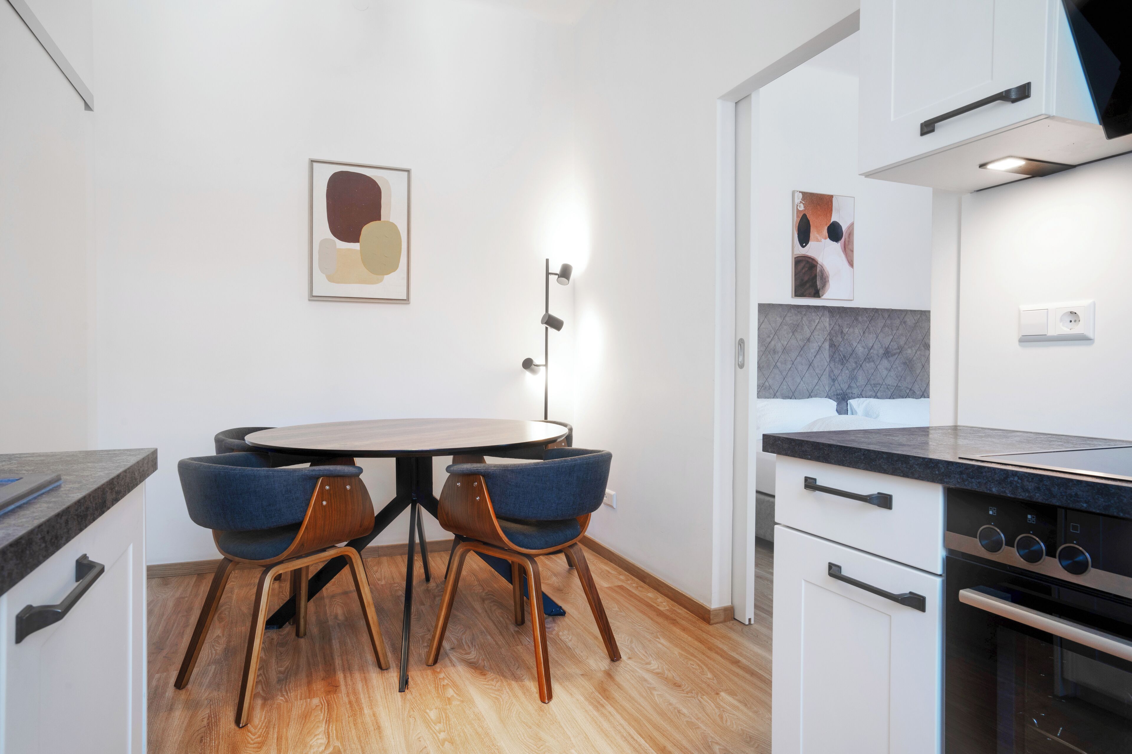 Een moderne keuken met een ronde eettafel, twee blauwe stoelen, witte kasten en een inbouwoven.