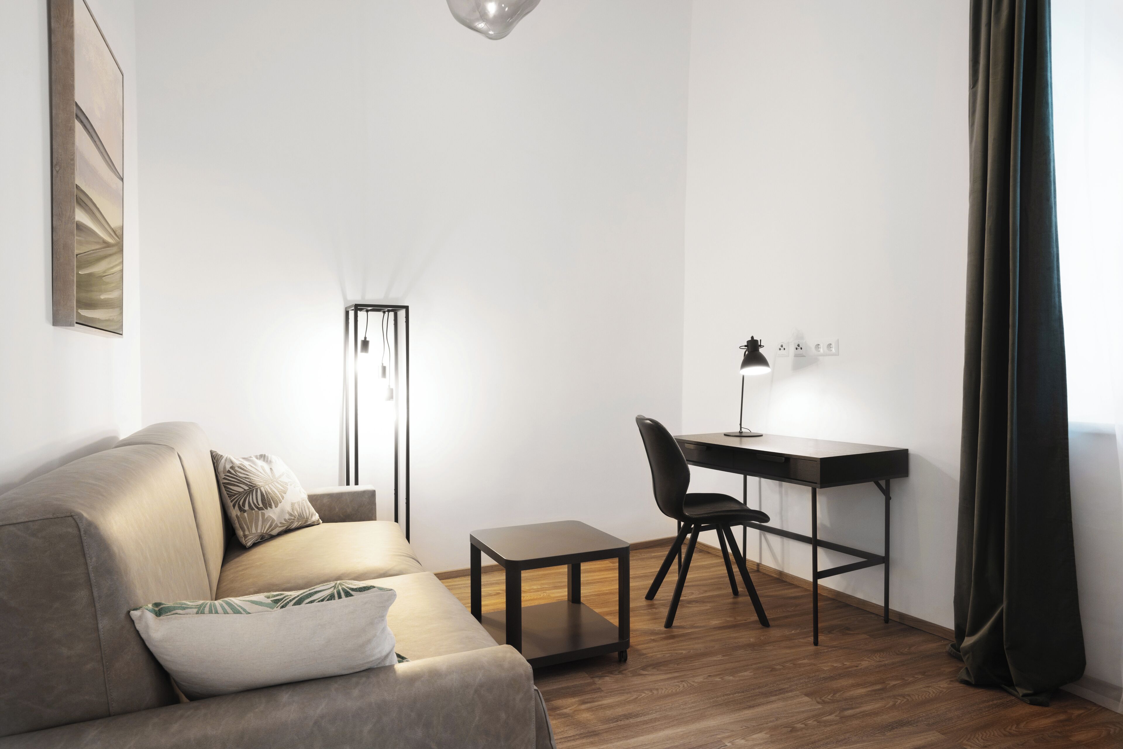 A modern living room with a sofa, a small table, a desk, and a floor lamp.