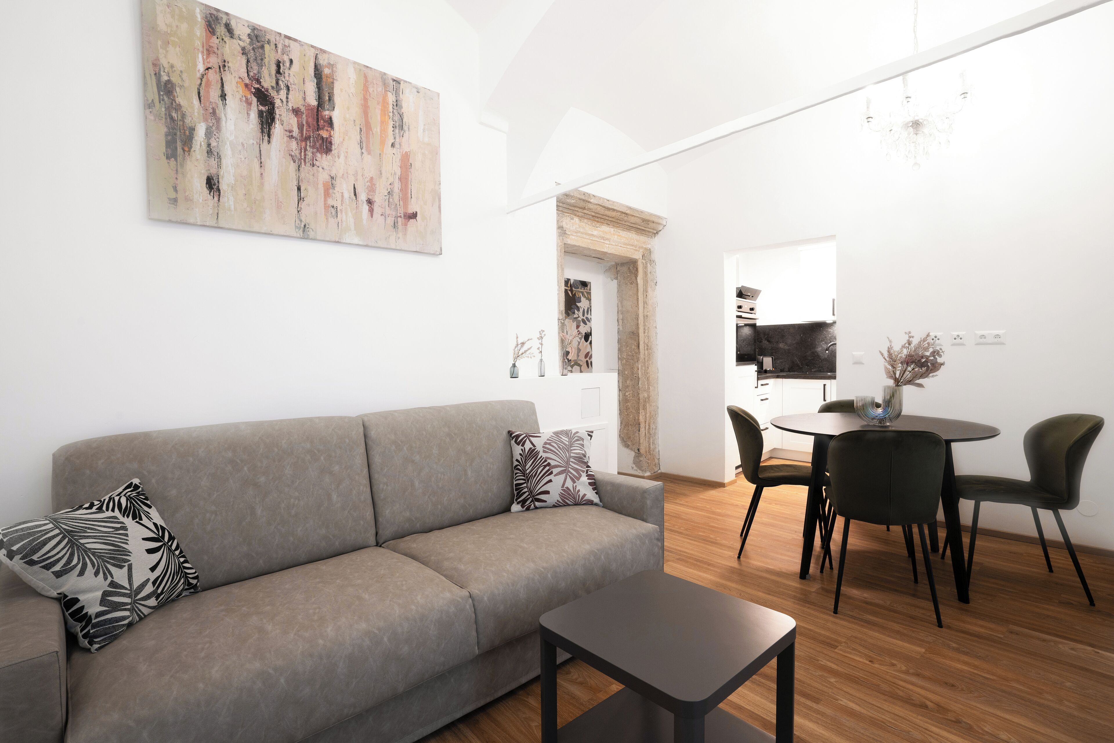 Un salon moderne avec un canapé gris, une petite table et un coin repas comprenant une table ronde et des chaises.